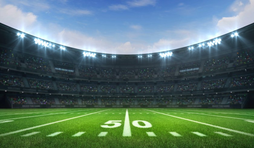 American football league stadium with white lines and fans, daytime side field view