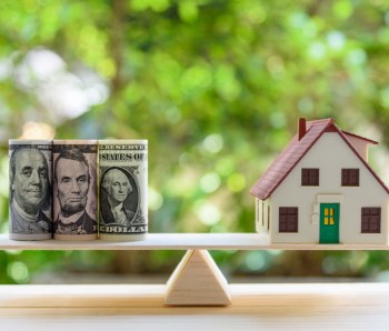 Home loan / reverse mortgage or transforming assets into cash concept : House model, US dollar notes on a simple balance scale, depicts a homeowner or a borrower turns properties / residence into cash