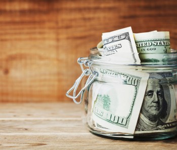 Dollar bills in glass jar on wooden background. Saving money concept.