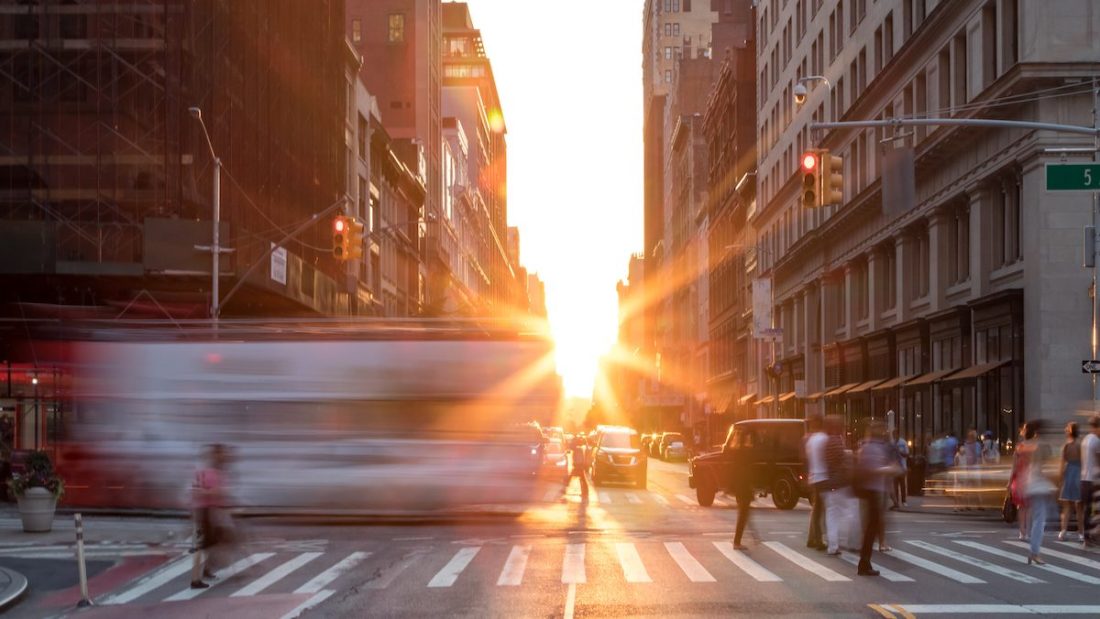 Busy New York City street scene with crowds of people in Midtown Manhattan with sunset background