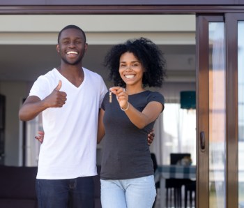 African couple standing on terrace hold keys of new house