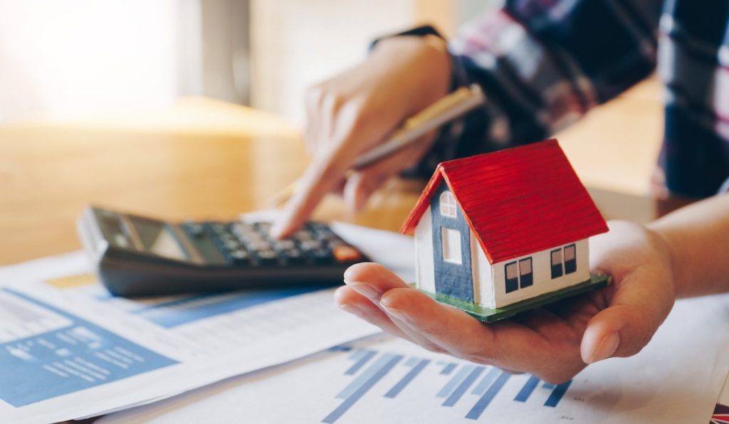 Woman holding house model in hand and calculating financial chart for investment to buying property.