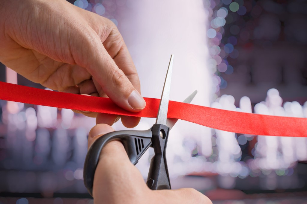 Man is cutting red tape or ribbon against defocused background.