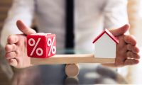 Close-up Of Wooden Seesaw Showing Balance Between Percentage Symbol And House Model Mortgage Rates