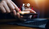 Businessman use smartphone with virtual home icon and down arrow for economical real estate and lower mortgage interest rates. Reduced prices for rental housing, Demand for home purchases decreases.