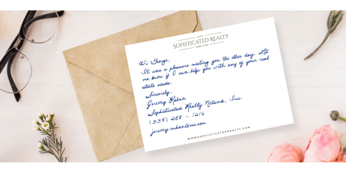 Brown envelope with a white handwritten postcard laying on top surrounded by flowers and a pair of reading glasses.